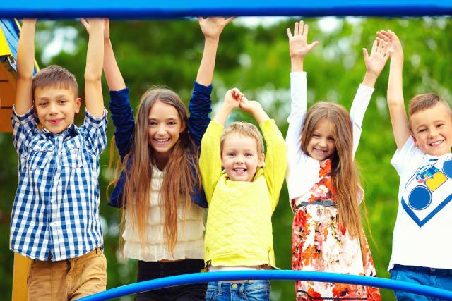 Cinq enfants souriants, les bras levés dans une aire de jeux extérieure